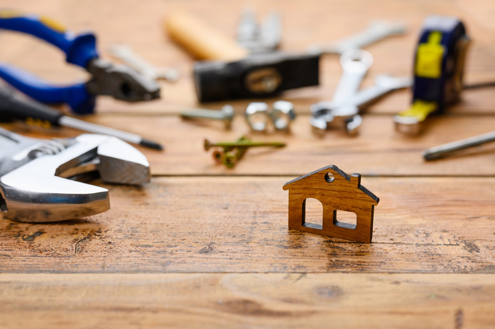 Small figurine of a house on the background of construction tools on a wooden table. House construction and renovation concept.